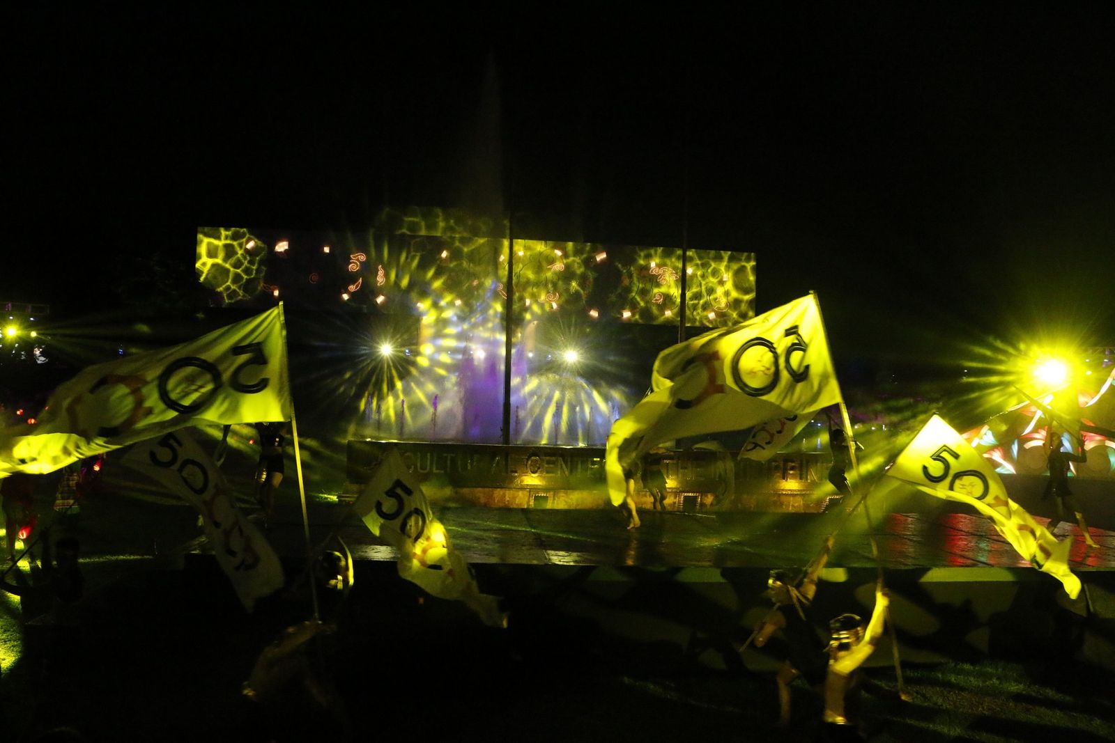 Dancers carrying 50th-anniversary flags in front of a lit water screen at the Cultural Center of the Philippines